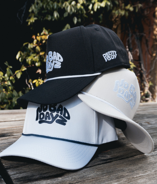 Different designs of "No bad dayz" hat stacked on a picnic table